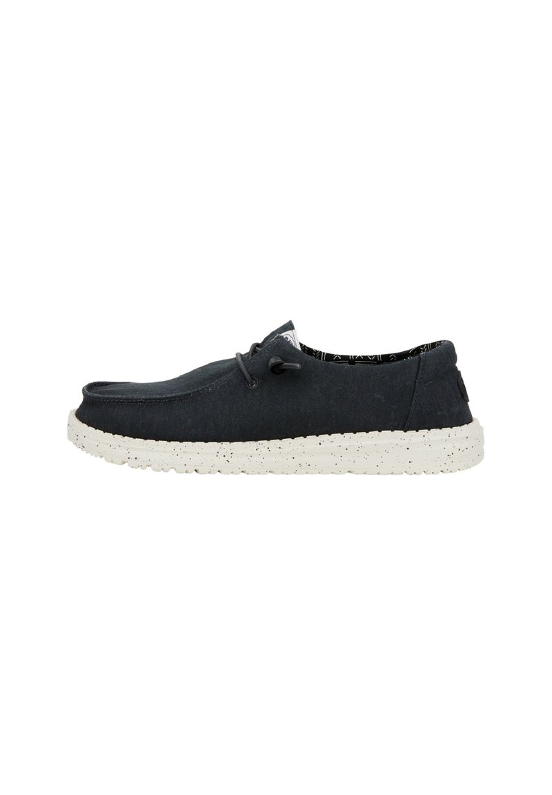 Zapatillas de lona azul marino oscuro con una suela blanca moteada. Entre sus características se incluyen un diseño minimalista, puntera redondeada y cierre con cordones.