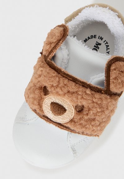 Chaussure pour bébé en thème d'ours brun doux avec un dessus moelleux, une semelle en cuir blanc et une sangle à boucle pour un enfilage facile. Fabriqué en Italie.
