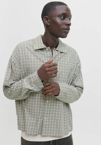 Grünes und weißes karriertes Hemd mit entspanntem Schnitt, langen Ärmeln und großem Kragen; der Stoff scheint leicht und mit einer weichen Textur zu sein.