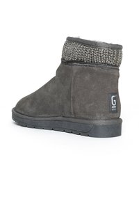 Bota de ante gris con un puño de punto, suela de goma y parche con logo. Presenta una textura suave y un diseño corto y redondeado.