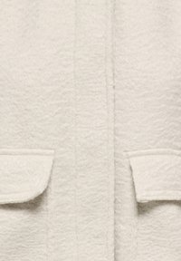 Nærbilde av kremfarget teksturert stoff med to klafflommer, som fremhever det myke, løkkeaktige ull-liknende materialet.