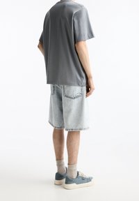 Camiseta de manga corta gris, pantalones cortos de mezclilla azul claro y zapatillas azules con suelas blancas y cordones beige. Diseño sencillo, ajuste casual.