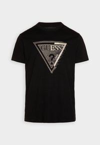 Schwarzes Baumwoll-T-Shirt mit einem dreieckigen silbernen Druck, der "GUESS®" und ein Fragezeichen zeigt. Rundhalsausschnitt, kurze Ärmel, glatte Textur.