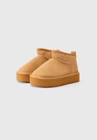 Botines de ante en tono marrón con forma redondeada, suela plana de goma y costuras visibles, con un corte bajo y una textura suave.