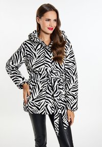 Veste à capuche imprimée zèbre en noir et blanc, avec une taille ceinturée, des manches longues et une texture douce. Pantalons noirs portés en dessous.