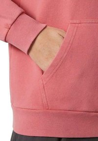 Sudadera rosa con una mezcla de algodón texturizada, que presenta un bolsillo tipo canguro en la parte delantera y puños de canalé. El dobladillo también es de canalé para un ajuste ceñido.
