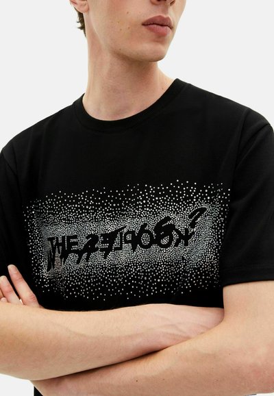 Juodas marškinėliai su tekstūruota grafika, sidabrinių taškų raštu ir ryškiu tekstu krūtinėje. Apvalus iškirpimas ir trumpomis rankovėmis.