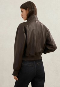 Jachetă maro din piele cu guler înalt, mansete și talie cu tiv striat. Textură netedă, design ajustat și siluetă scurtă.