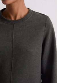 Sweatshirt gris foncé avec un col arrondi, tissu texturé et détails de couture subtils le long des coutures des épaules et du corps.