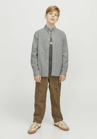 Camicia a quadri in bianco e nero sopra una t-shirt grigia, abbinata a pantaloni cargo color khaki e sneakers beige.