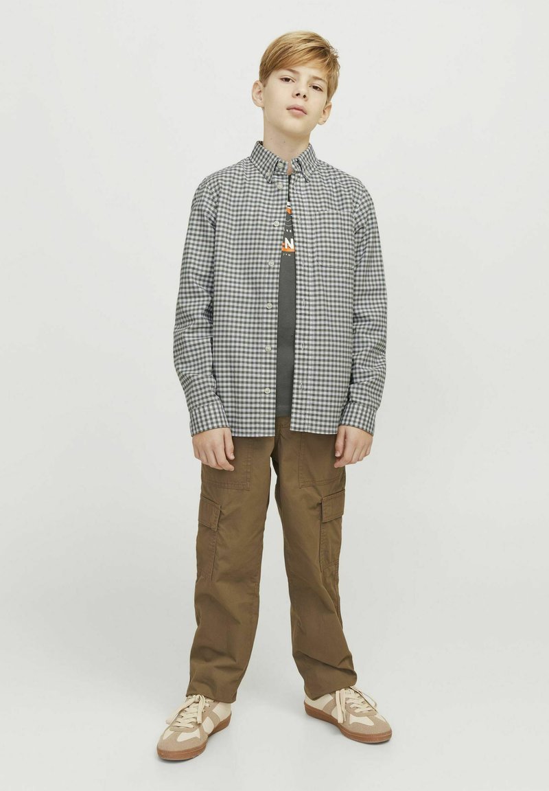 Camicia a quadri in bianco e nero sopra una t-shirt grigia, abbinata a pantaloni cargo color khaki e sneakers beige.