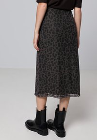 Jupe midi imprimée léopard avec un revêtement transparent, dans des couleurs noir et gris foncé, associée à des bottines noires à cheville avec des panneaux élastiques sur les côtés.