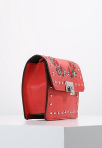Borsa a tracolla rossa in pelle sintetica con un motivo decorativo di rose ricamate, borchie silver e chiusura a morsetto in metallo. Forma rettangolare con una struttura rigida.