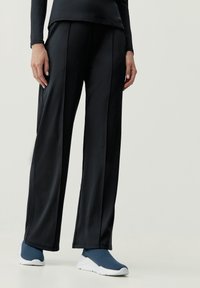 Czarne sportowe spodnie o szerokim kroju, gładkiej fakturze i subtelnych detalach szwów, zestawione z niebieskimi butami wsuwanymi.