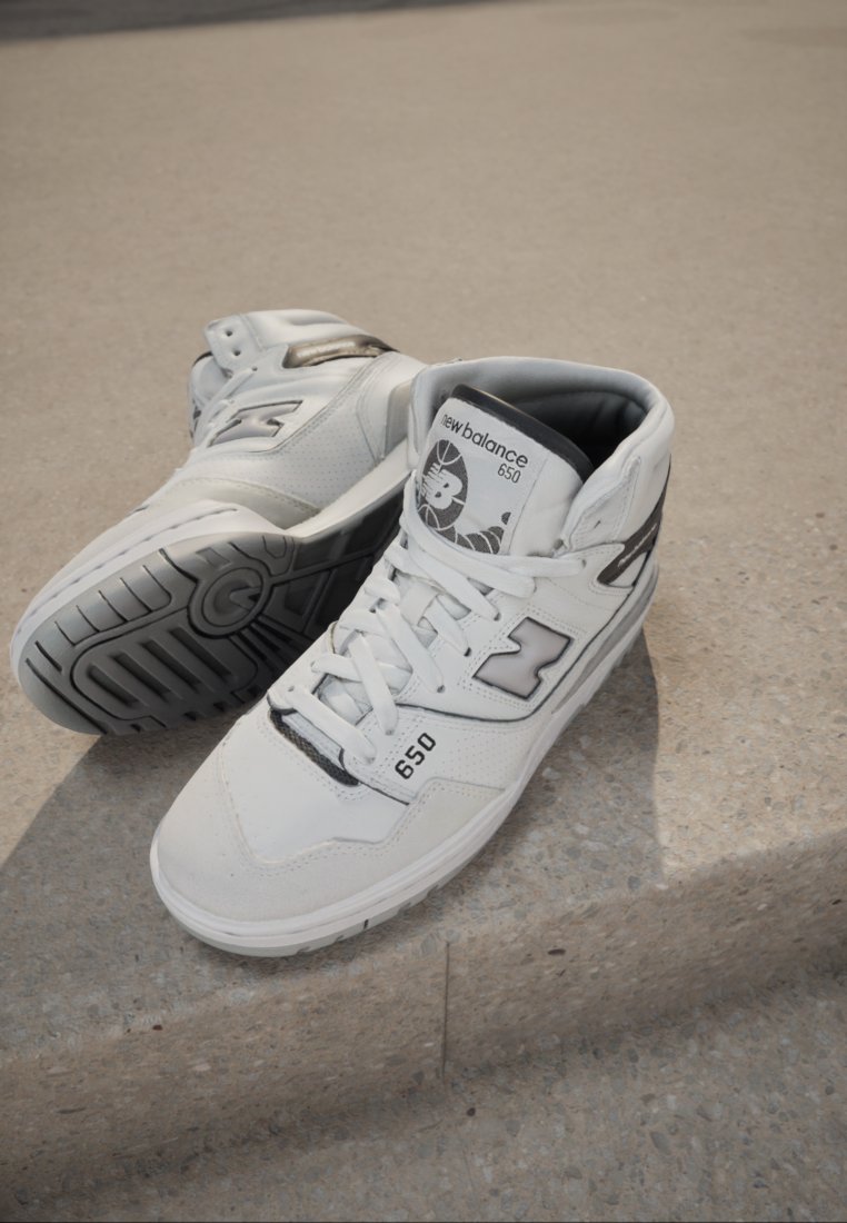 Weiße High-Top-Sneaker aus Leder und synthetischen Materialien mit schwarzen Akzenten, ausgestattet mit Schnürsenkeln, einem gepolsterten Kragen und strukturierten Gummisohlen.