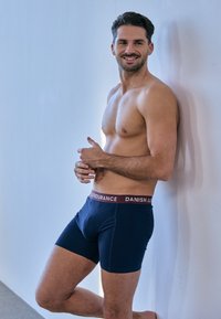 Boxer briefs blu scuro con una fascia elastica marrone recante il testo "DANISH ENDURANCE". Tessuto liscio, design aderente, senza motivi visibili.