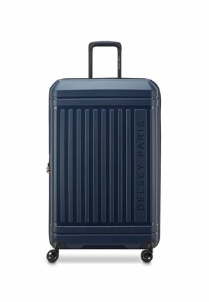 Valigia rigida a rotelle di colore blu navy, con linee verticali, manico telescopico, quattro ruote e marchio in rilievo "DELSY PARIS".