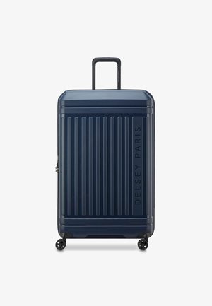 Maleta rígida con ruedas en azul marino que presenta líneas verticales, un mango telescópico, cuatro ruedas y el logotipo en relieve "DELSY PARIS".