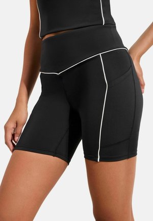 Black athletic shorts made of stretchy fabric, featuring white piping along the seams and a high waistband with a smooth finish.