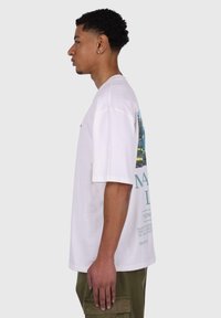 White cotton t-shirt with short sleeves, featuring a colorful graphic print on the back and text design in teal. Casual fit, soft texture.
