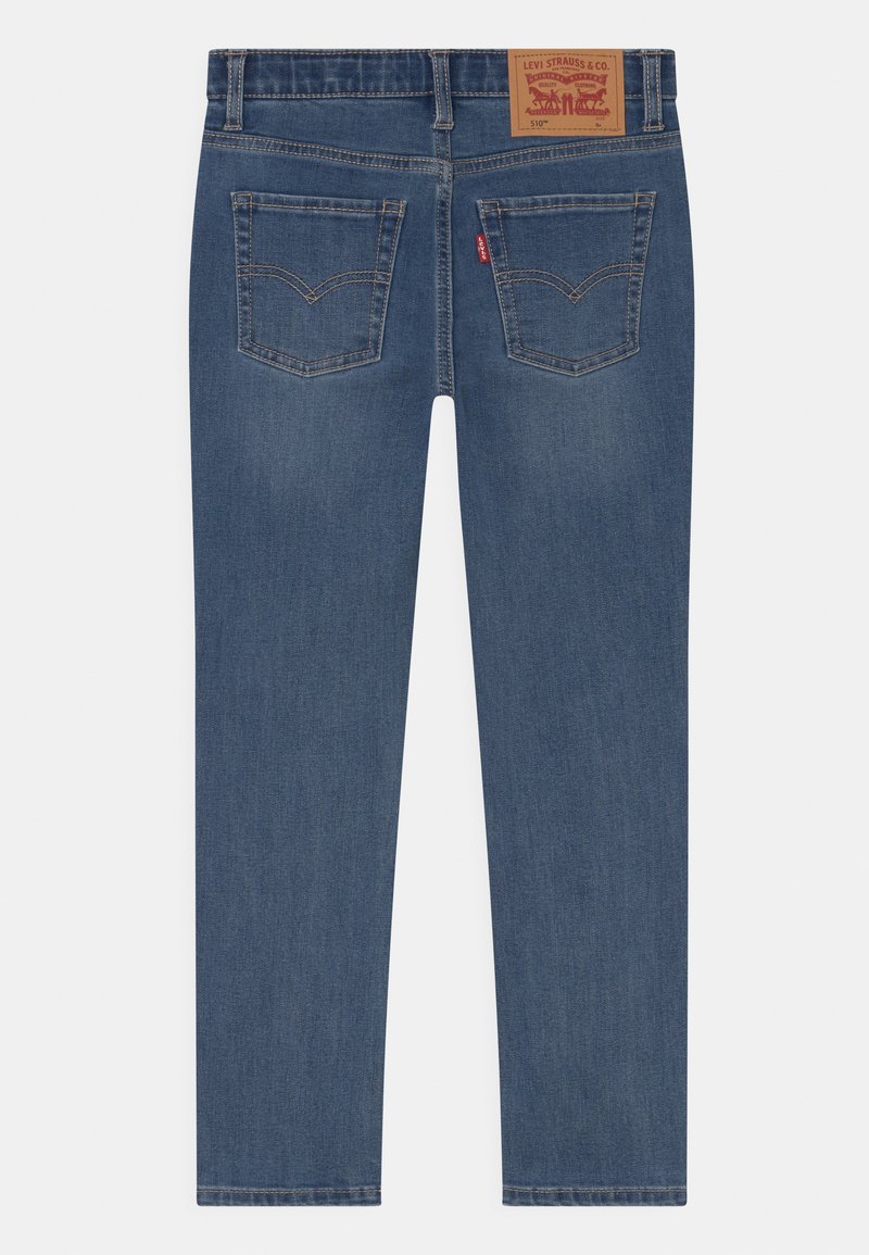 Jeans de mezclilla azul con corte recto, que cuentan con un parche de cuero en la cintura y dos bolsillos traseros con detalles de costura.