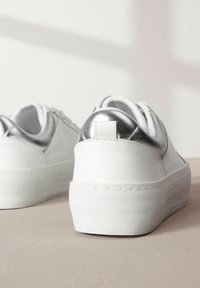 Adidași albi cu toc metalic argintiu, talpă platformă texturată albă și șireturi rotunde. Partea superioară din piele netedă cu un design minimalist.