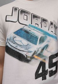 Camiseta de algodón blanca con un gráfico de un coche de carreras que lleva los números "45" y "JORDAN" en texto negro en negrita, con una combinación de colores azul y gris.