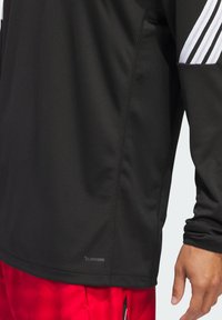 Čierne športové tričko s dlhým rukávom z priedušnej tkaniny, ktoré má textúrovaný dizajn a biele pruhy na rukávoch. Viditeľné logo ClimaCool.