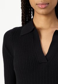 Black ribbed sweater featuring a V-neck and a collar, close-fitting design, with a soft texture. The sweater's fabric appears smooth and cozy.