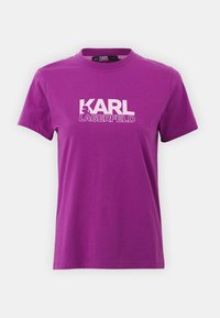 Camiseta de algodón morada con mangas cortas, cuello redondo y texto gráfico en blanco "KARL LAGERFELD". Textura suave sin patrones.