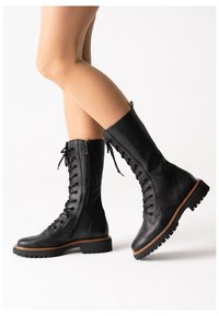 Botas de tobillo de cuero negro con cordones y cremallera lateral, suela robusta y detalles de costura a lo largo de la plataforma. Acabado texturizado y diseño resistente.