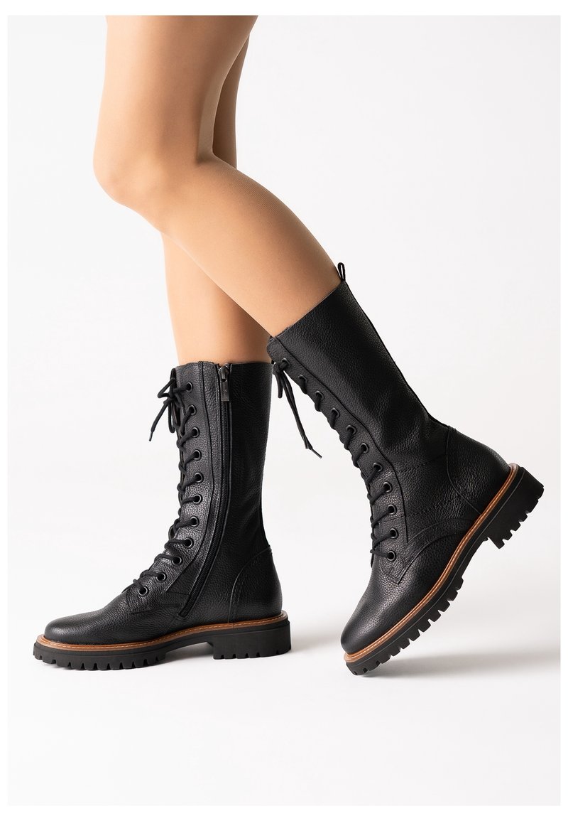 Botas de tobillo de cuero negro con cordones y cremallera lateral, suela robusta y detalles de costura a lo largo de la plataforma. Acabado texturizado y diseño resistente.