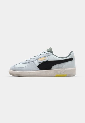 Zapato deportivo azul claro con material de ante, franja lateral negra, acentos grises, suela de goma blanca y marca Puma en la lengüeta y el talón.