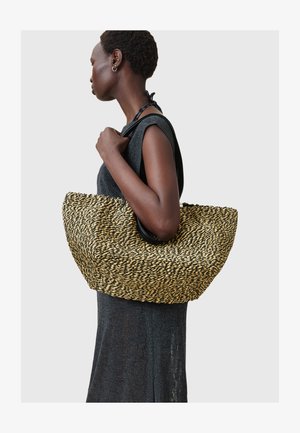 Borsa tote intrecciata in paglia con manico nero, caratterizzata da una forma arrotondata, filamenti alternati neri e gialli e una superficie testurizzata.