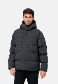 Doudoune noire avec un col montant, deux poches zippées à l'avant, motif matelassé et coupe ample. Équipée d'une capuche et de poignets élastiques.