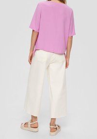 Haut rose à manches courtes avec un ourlet arrondi, associé à un pantalon large blanc. Les sandales présentent un design tressé et une semelle épaisse.