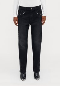 Jeans negri din denim cu tăietură dreaptă, decorate cu cuie argintii pe buzunare și pe laterale. Purtați cu pantofi cu toc ascuțit negri.