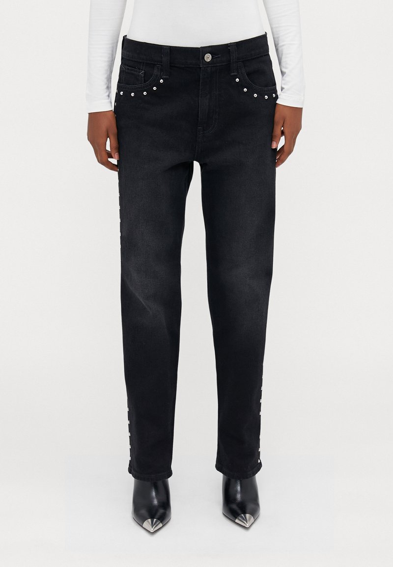 Jeans negri din denim cu tăietură dreaptă, decorate cu cuie argintii pe buzunare și pe laterale. Purtați cu pantofi cu toc ascuțit negri.