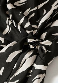 Tissu noir avec de larges rayures blanches abstraites, noué au centre, mettant en valeur une texture lisse et un design à fort contraste.