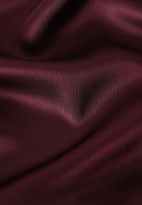 Tissu satin lisse et profond de couleur bordeaux avec des plis doux et un subtil éclat brillant reflétant la lumière sur sa surface texturée.