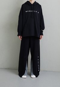 Felpa nera oversize con stampa "MARGIELA 6" e pantaloni della tuta larghi abbinati con pannelli laterali grigi. Tessuto morbido, vestibilità casual.
