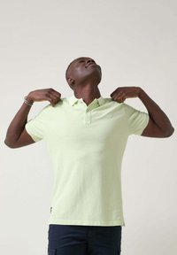 Polo verde claro de tela suave, con cuello, tres botones y mangas cortas. Logotipo sutil en el pecho, ajuste relajado.