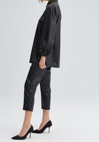 Svart satin topp med ballongärmar och krage, kombinerad med svarta fusk läder beskurna byxor med sömsömnad, och svarta stilettklackar.