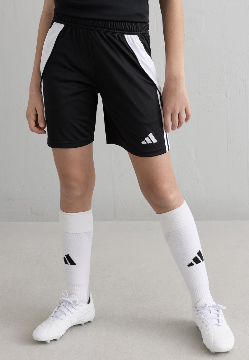 Melni sporta šorti ar baltām sānu svītrām, elastīga josta un Adidas logotips. Apvienoti ar baltām ceļgalu zeķēm un baltām sporta kurpēm.