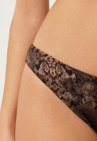 Bikini kalhotky s hnědým hadím vzorem a nízkým pasem, s hladkou texturou a tenkým páskem, která ukazuje vzor inspirovaný plazy.