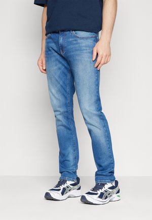 Vaqueros de mezclilla azul claro con un corte ajustado, que cuentan con cinco bolsillos y un desvanecimiento sutil. Combinados con zapatillas blancas y navy.