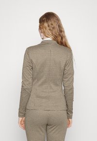 Blazer ajusté à carreaux marron et beige, en tissu texturé. Il présente un col cranté et des manches étroites.