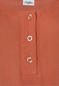 Blůza v rezavé barvě s texturovanou tkaninou a knoflíkovou légu se třemi kulatými, průhlednými knoflíky. Na štítku je nápis "Buffalo."