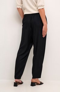 Schwarze, locker sitzende Hosen mit elastischem Bund, aus leichtem Stoff gefertigt. Mit schmal zulaufenden Knöcheln und einer glatten Oberfläche.