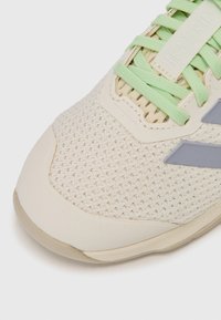 Light beige athletic shoe featuring a textured mesh upper, green laces, and grey accents on the side. Soft rubber sole with a sleek design.
